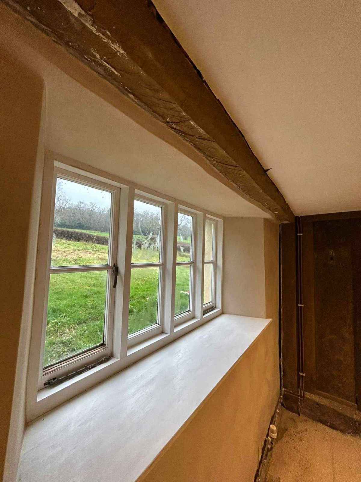 A deep cottage window reveal freshly plastered under an old beam
