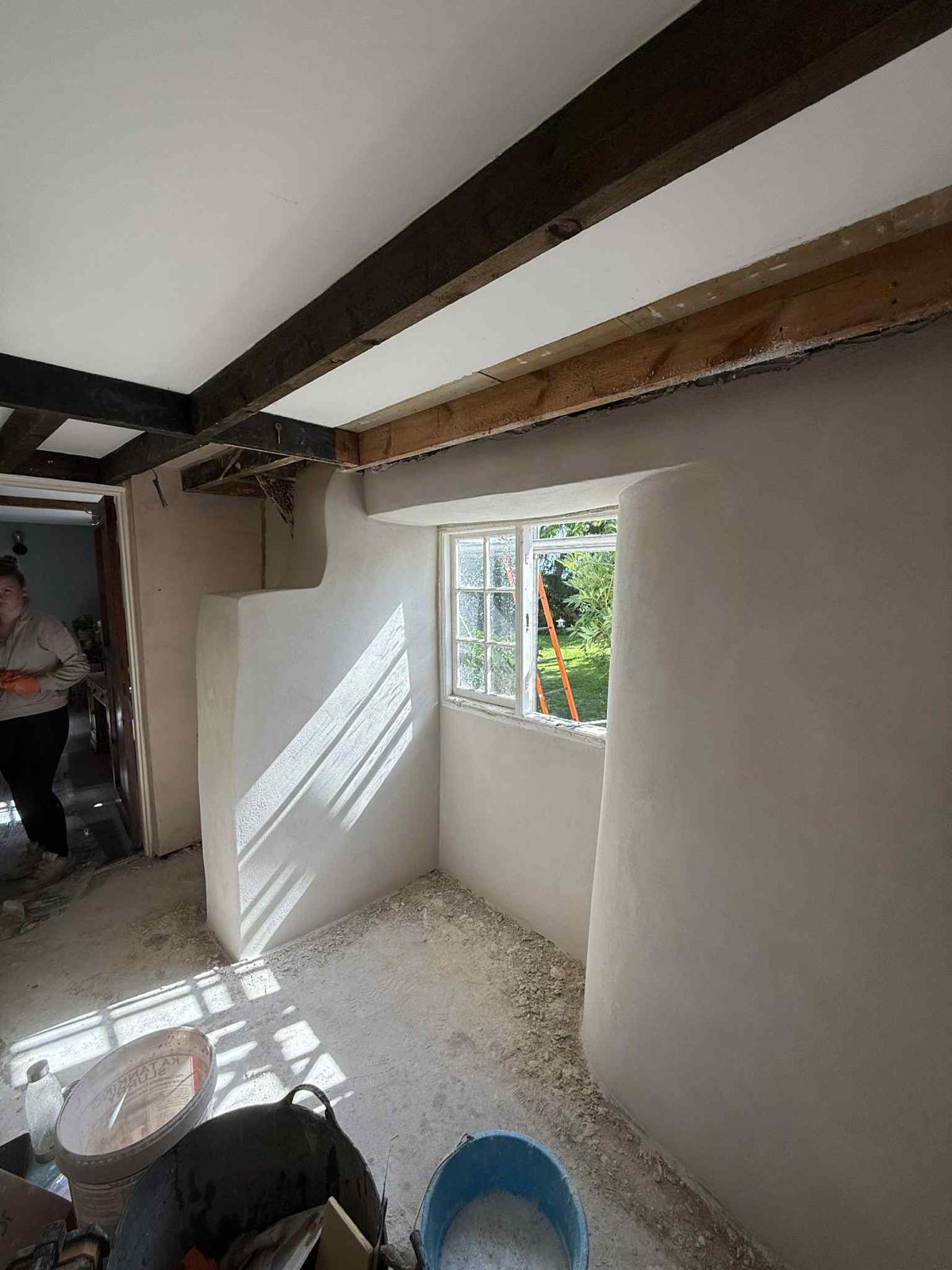 A curved plastered wall under old beams, work in progress